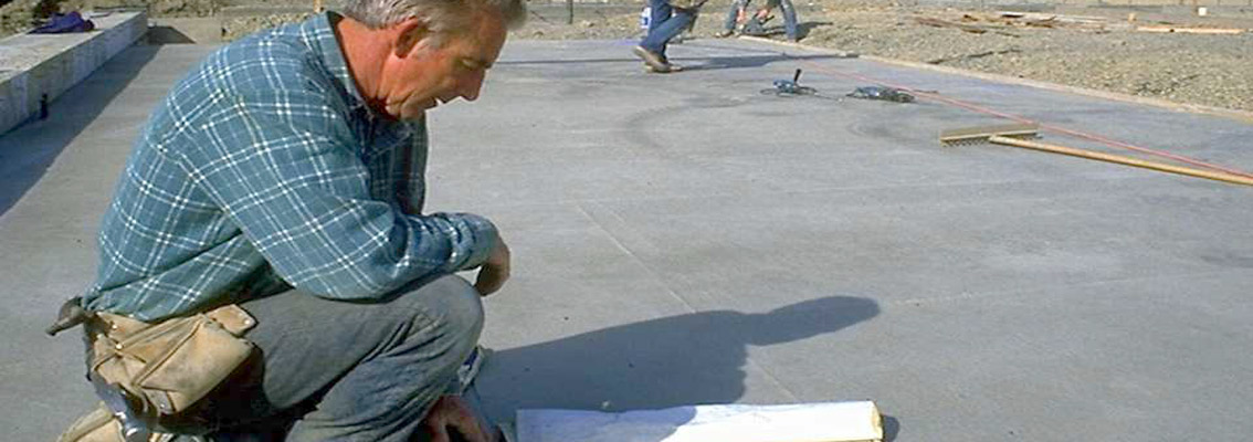 Construction Worker kneeling on concrete looking at blueprints