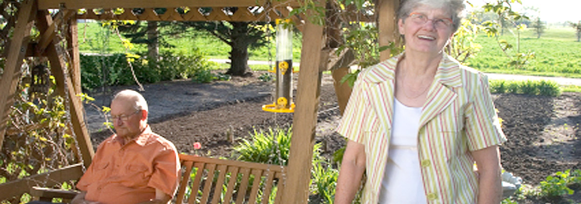 Elderly man on sitting on swing with wife standing